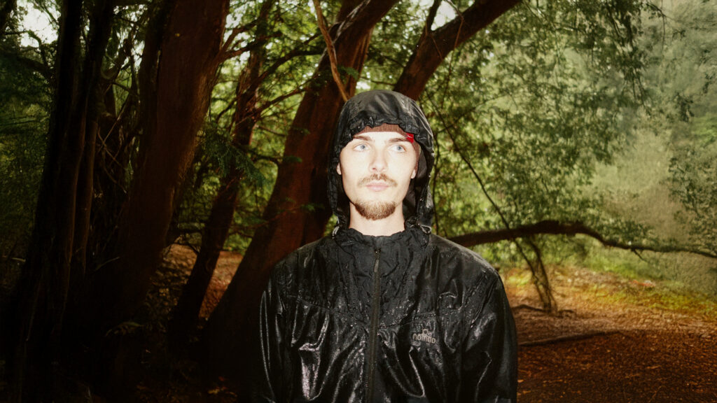Simeon, Amsterdam-born alternative hip-hop artist, standing in a forest for a press photo.